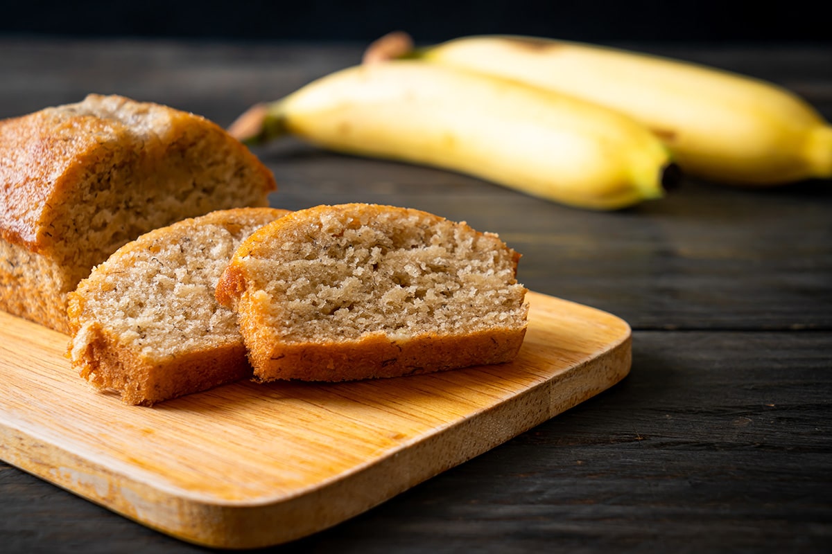 bolo de banana sobre uma tábua com bananas ao fundo